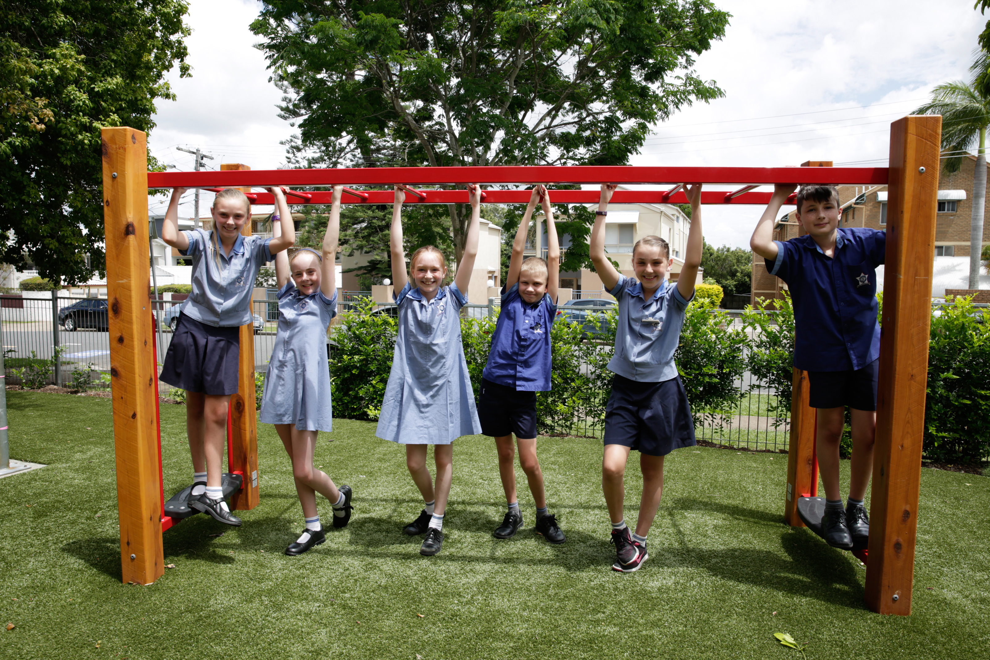 Students in school uniform using monkey bars on a grassed outdoor playground.